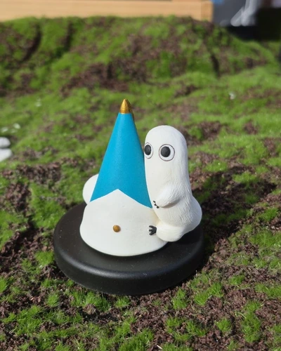 Figura del Gusano Pincel de Atelier of Witch Hat junto a un sombrero azul, fotografiada en exterior