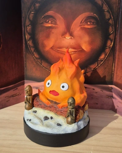Primer plano de la figura de Calcifer con llamas naranjas y dos figuras decorativas a los lados